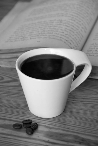 Een kopje hete zwarte koffie close-up naast gebrande koffiebonen en open boek. Ochtend kopje koffie. - Foto, afbeelding