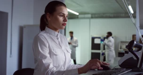 Side view of Caucasian beautiful young woman professional laboratory assistant sits in office and typing on keyboard working searching for analysis. Female microbiology scientist at workplace Portrait - Footage, Video