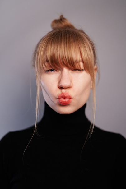Cheerful smiling fashion girl in casual black sweater with red lips on gray background looking at camera and making a duck face - Photo, Image