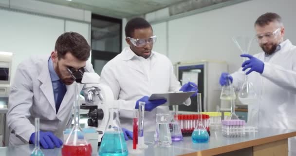 Retrato de científicos de microbiología masculina de razas mixtas que trabajan en un laboratorio médico moderno realizando experimentos genéticos utilizando equipos profesionales de microscopio que examinan los resultados de la escritura de muestras de vacunas - Metraje, vídeo