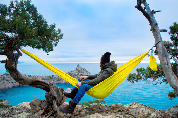 Vrouw ontspannen in de gele turquoise hangmat tegen de achtergrond van een prachtig landschap. Concept van ontspanning en meditatie. De zuidkust van de Krim in de winter. Nieuwe wereld Novy Svet - Foto, afbeelding