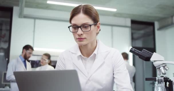 Közelkép kaukázusi gyönyörű fiatal elfoglalt komoly női orvos szemüveges ül íróasztal a kórházban laboratóriumi böngészés laptop, szörfözés interneten a számítógépen a munkahelyen. Laboratóriumi koncepció - Felvétel, videó