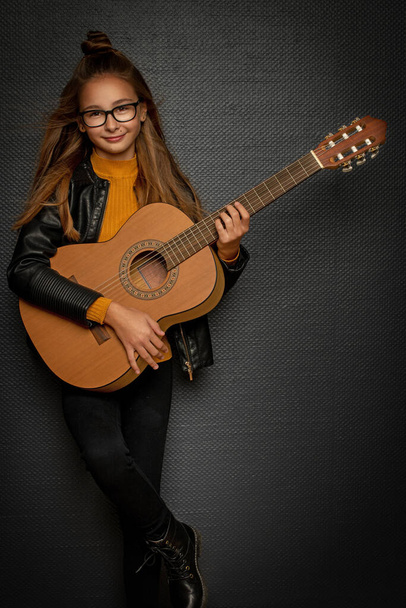 Little blonde girl playing guitar on black background - Fotoğraf, Görsel