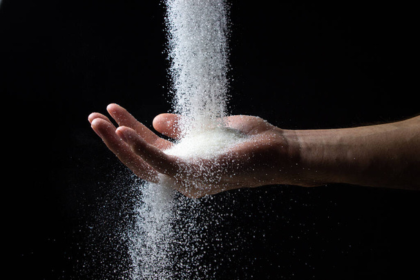 Sokeria mustalla pohjalla. Sokeri kaadetaan miehen käteen. Liiallinen sokerin saanti - Valokuva, kuva