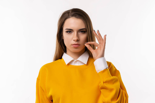 Your secrets safe with me concept. Brunette girl in casual clothes showing zip gesture as if shutting mouth on key. Studio shot, white background. Keep a secret - Foto, imagen