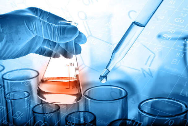 рука ученого, держащего фляжку с лабораторным стеклом на фоне химической лаборатории, концепция научных лабораторных исследований и разработок  - Фото, изображение