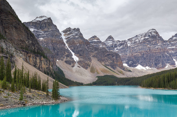 美しいターコイズブルーの水は、カナダのアルバータ州モレーン湖で夏の朝にタイガの森と岩の山に囲まれています - 写真・画像