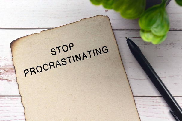 Tekst op gebrand bruin papier met pen en wazig groene plant op houten bureau - Stop Procrastinating - Foto, afbeelding