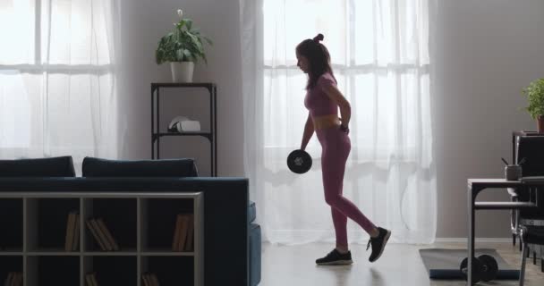 Αθλητική γυναίκα κάνει ασκήσεις με βάρος, προπόνηση μόνη στο σπίτι, γέρνει προς τα εμπρός και κινείται πόδι προς τα πάνω, λεπτή γυναικεία φιγούρα - Πλάνα, βίντεο