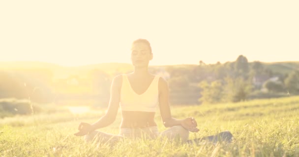 Yogi feminino caucasiano sentado na grama com os olhos fechados e meditando em pose de lótus. Yoga asana para meditação. De manhã cedo. Retrato de bela mulher feliz abrindo os olhos e sorrindo para a câmera. - Filmagem, Vídeo