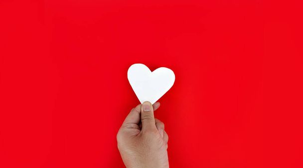 Hand met een wit hart op een rode achtergrond De betekenis van ware liefde is de beste wensen voor degenen van wie ze houden, de vreugde waarmee de geliefden gelukkig zijn. - Foto, afbeelding