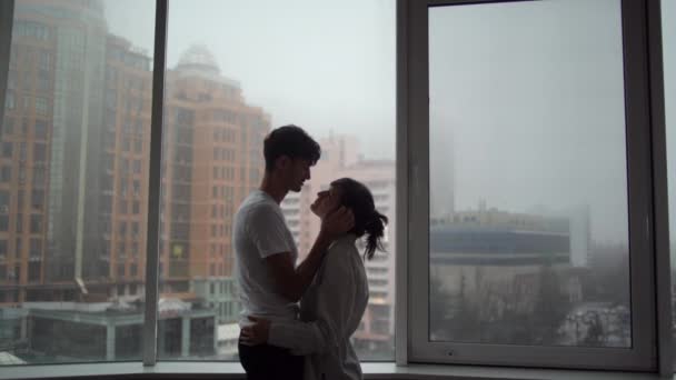Una pareja sexy y cariñosa de etnia caucásica abraza y besa apasionadamente contra el fondo de ventanas panorámicas en apartamentos. - Imágenes, Vídeo