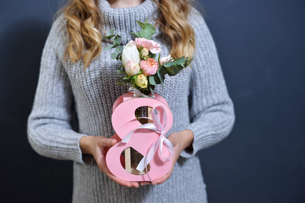 una ragazza bionda con un maglione grigio tiene in mano un mazzo di fiori nel video numero otto. regalo per la giornata internazionale della donna. - Foto, immagini