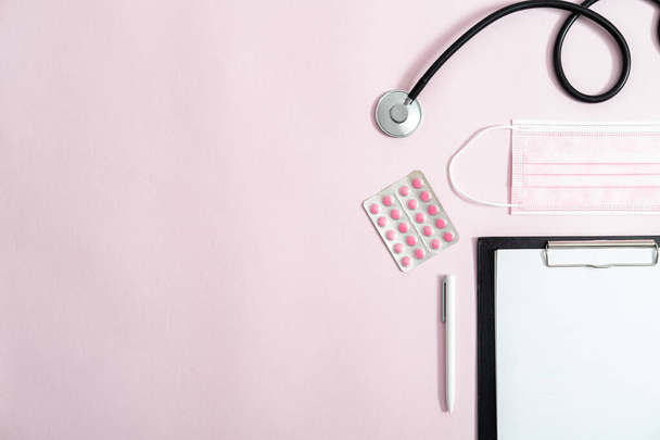 Stethoscoop, roze chirurgisch masker, roze pillen, klembord en pen op roze achtergrond met kopieerruimte - Foto, afbeelding