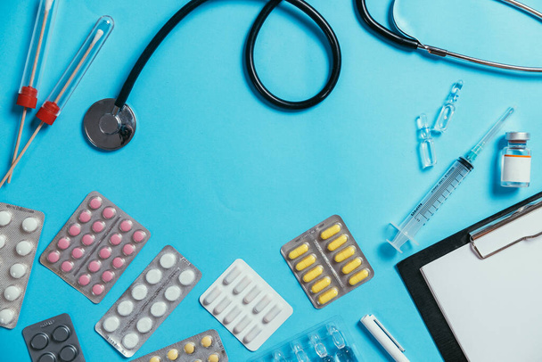 Orvosi felszerelés kék háttérrel. Lapos laikus sztetoszkóp, tampon, tabletták, fecskendő, vakcina, ampullák és írótábla. Orvosi banner sablon másolási hellyel, header mockup - Fotó, kép