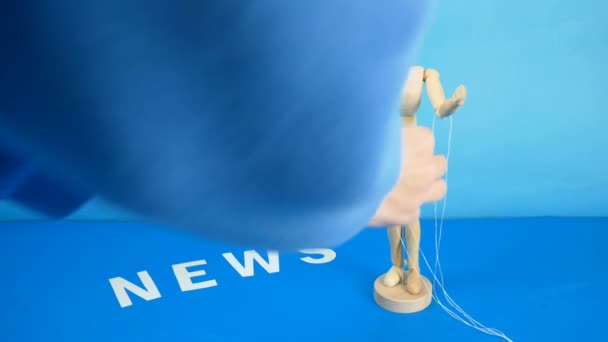 Steuerung einer Marionette durch Saiten an den Fingern und Word News auf blauem Hintergrund - Filmmaterial, Video