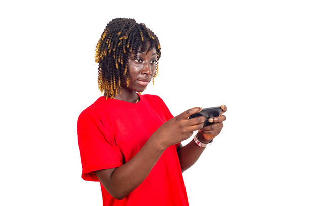 une belle jeune femme en t-shirt rouge debout sur un fond blanc tenant son téléphone portable et regardant ailleurs. - Photo, image