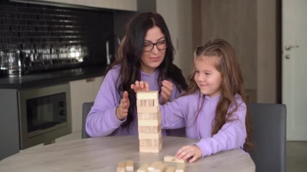 Jonge brunette moeder draagt bril speelt een houten bordspel met haar dochtertje 5 jaar oud. Moederschap en kindertijd. - Video