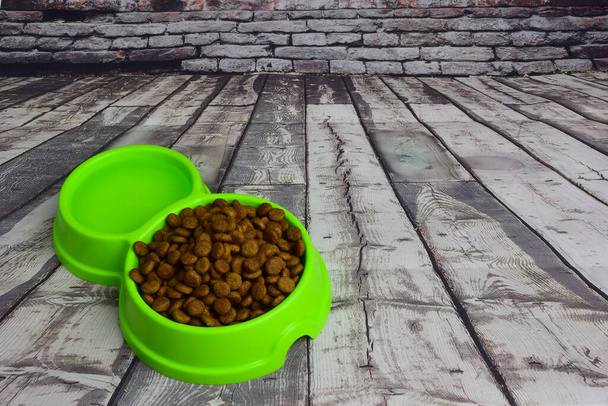 Contra um fundo de tábuas de madeira cinza, encontra-se uma placa de plástico verde cheia de alimentos secos para alimentar gatos ou cães. Há um lugar à direita para uma inscrição - Foto, Imagem