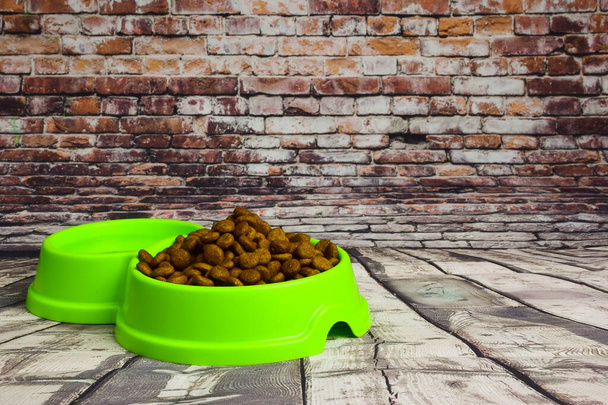 Contra um fundo de tábuas de madeira cinza, encontra-se uma placa de plástico verde cheia de alimentos secos para alimentar gatos ou cães. Há um lugar à direita para uma inscrição - Foto, Imagem