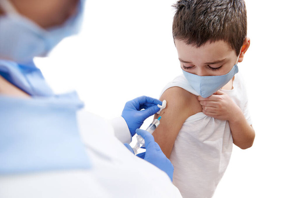 De bange jongen kijkt naar zijn hand terwijl de dokter hem vaccineert. Geïsoleerd op een witte achtergrond - Foto, afbeelding