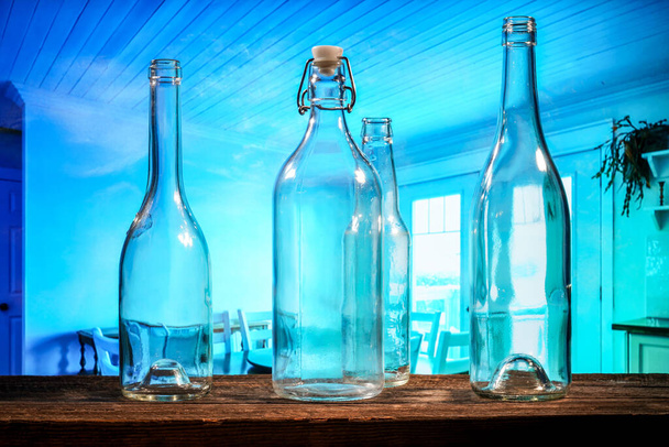 Čtyři průhledné skleněné láhve na hnědé stodole dřevěný stůl před modrým pozadím - Fotografie, Obrázek