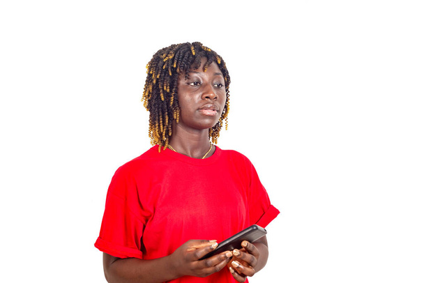 krásná mladá žena v červeném tričku stojící na bílém pozadí přemýšlející o tom, zatímco drží mobil. - Fotografie, Obrázek