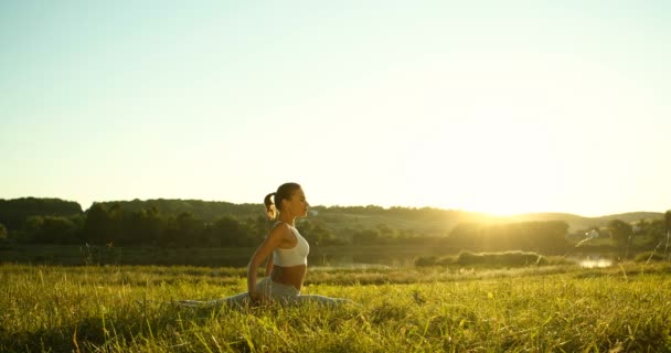 Yogui femenino joven caucásico acostado sobre hierba verde, meditando y respirando. Hermosa naturaleza rural. Mujer deportiva en yoga asana comenzando el día de verano temprano en la mañana mientras se estira. - Metraje, vídeo