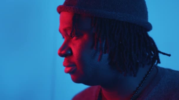 Profil młodego afrykańskiego czarnego mężczyzny z dredami oświetlonymi czerwonym i niebieskim światłem - Materiał filmowy, wideo