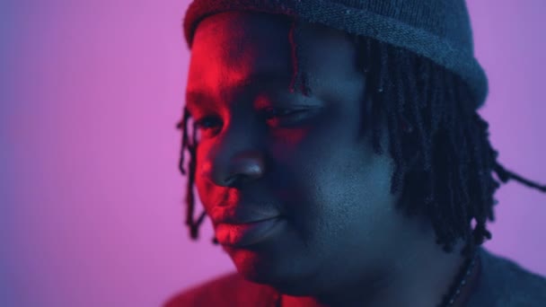 Pensativo joven afroamericano negro iluminado con luz roja y azul. Expresión de la cara cercana - Metraje, vídeo