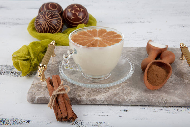 Cup of salep milky hot drink of Turkey with cinnamon powder and  healthy spice and autumn winter iecei on white rustic vintage wooden table.  - Photo, Image