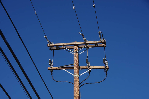Niski kąt widzenia zbliżenie słupa dystrybucji energii elektrycznej pod jasnym błękitnym niebem - Zdjęcie, obraz