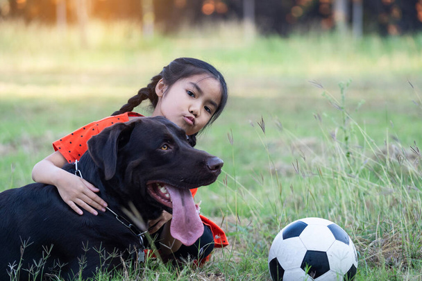 Une jeune fille Asain jouant au football avec son gros chien noir à l'extérieur de la pelouse dans la cour le soir.  - Photo, image