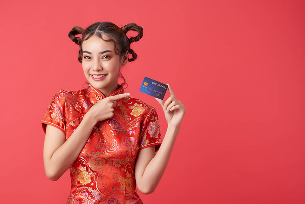 hermosa mujer asiática vistiendo tradicional cheongsam qipao vestido mostrando tarjeta de crédito sobre fondo rojo para chino conceptos de compras de año nuevo - Foto, Imagen