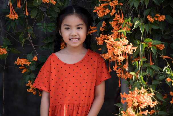 Portrait d'une jeune fille asiatique maigre et joyeuse jouit de fleurs à l'extérieur de la cour du jardin le soir. Une fille asiatique en tenue rouge pour célébrer la nouvelle année chinoise. - Photo, image
