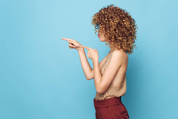 女性の肖像画カーリーヘアサイドビューのジェスチャーで指をコピースペースブラウンパンツ  - 写真・画像