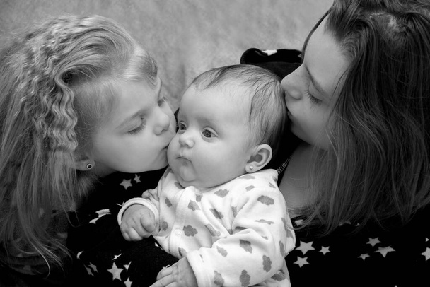 İki kız kardeş sarılıp en küçüğü öper. Mutlu kızlar ailesi. - Fotoğraf, Görsel