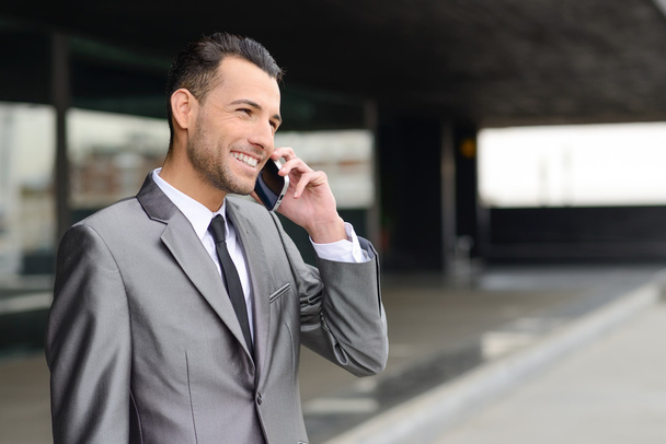 Привлекательный молодой бизнесмен по телефону в офисном здании
 - Фото, изображение