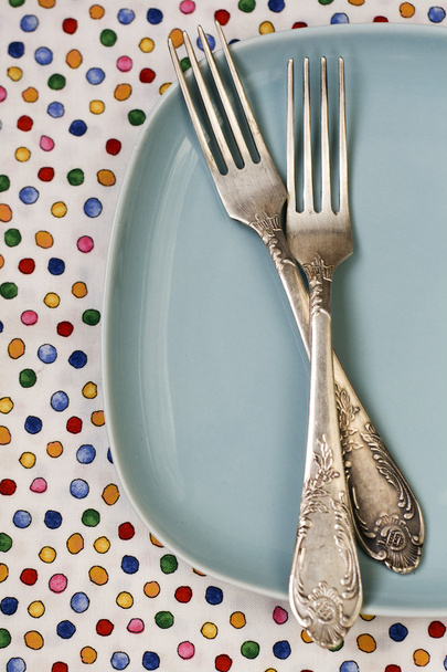 Dos tenedores acostados sobre un plato azul sobre un fondo brillante
 - Foto, imagen