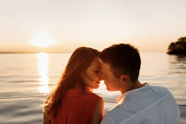 Sanfte und rührende Umarmungen auf einer Jacht vor dem Hintergrund des Wassers im Meer, ein verliebtes Paar bei Sonnenuntergang. . Hochwertiges Foto - Foto, Bild