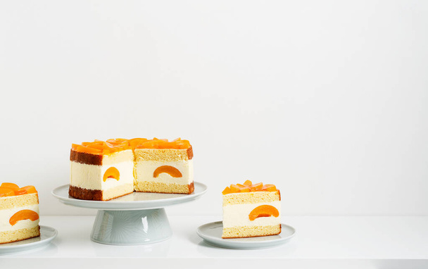 Mehrschichtiger Käsekuchen mit Pfirsichen auf Kuchenständer, weißer Hintergrund. - Foto, Bild