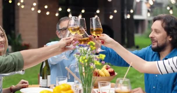 Cheerful happy Caucasian family sitting at table outdoors, having dinner and cheering with drinks while toasting. Joyful parents with children spending weekend together and celebrating. - Footage, Video