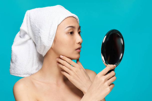 жінка азіатського вигляду голі плечі дзеркало в руках чистий синій фон шкіри
 - Фото, зображення