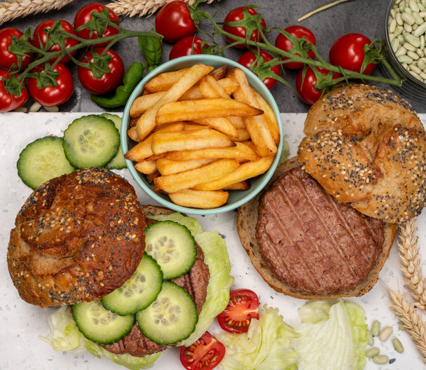 Vaření chutného vegetariánského veganského oběda s hamburgerem z rostlinných sójových bobů burger, bio houska se semínky a čerstvá zahradní zelenina a smažené brambory - Fotografie, Obrázek