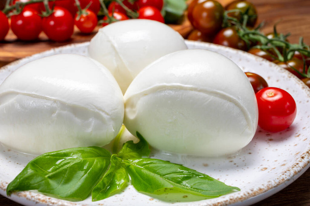 Коллекция сыра, белые шарики мягкого итальянского сыра моцарелла, подается с красными помидорами черри, свежие листья базилика близко - Фото, изображение