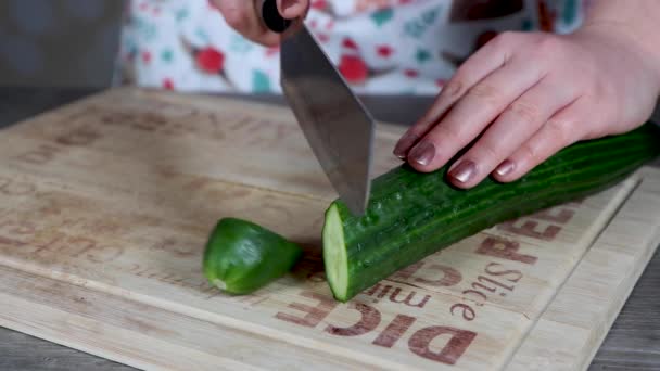 Mutfakta bir kadın salatalığı dilimleyip tahta kesme tahtasına koyuyor. Ev yemeği kavramı. - Video, Çekim