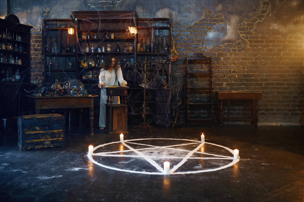 Young demonic woman reads book of spells, demons casting out. Exorcism, mystery paranormal ritual, dark religion, night horror, potions on shelf on background - Photo, Image