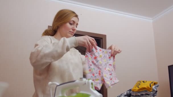 Giovane madre stirare vestiti per bambini - Filmati, video