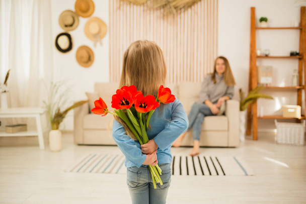A kislány vörös tulipánt ad az anyjának a szobában. Nemzetközi nőnap - Fotó, kép