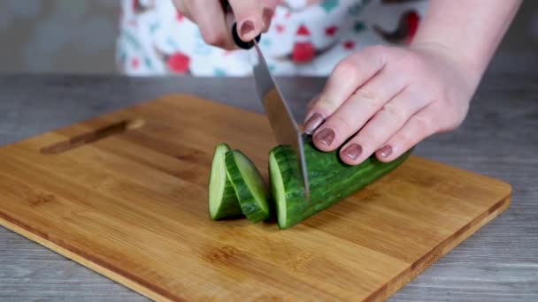 A woman in a kitchen cutting up a cucumber in to slices on a wooden chopping board, home cooking concept - Footage, Video